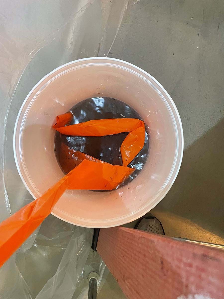 A plastic cup filled with a brown liquid and an orange ribbon.