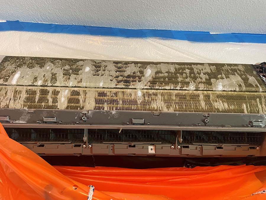 A dirty air conditioner is sitting on top of an orange tarp.