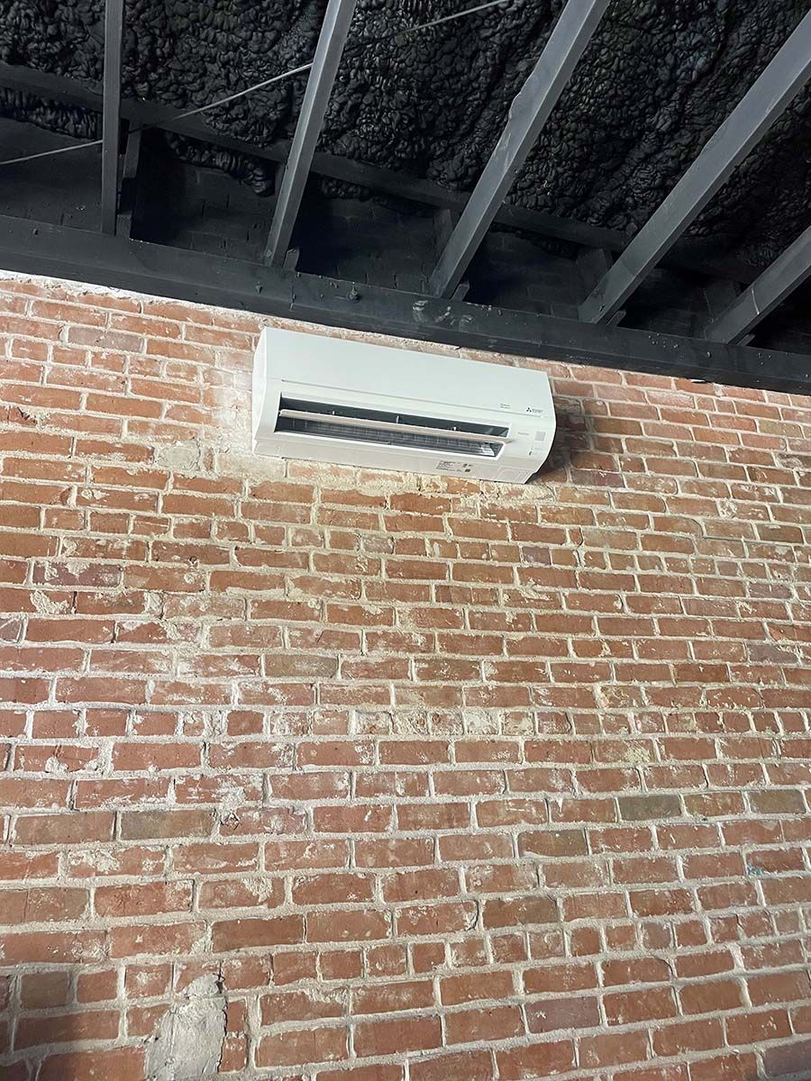 A white air conditioner is mounted on a brick wall.
