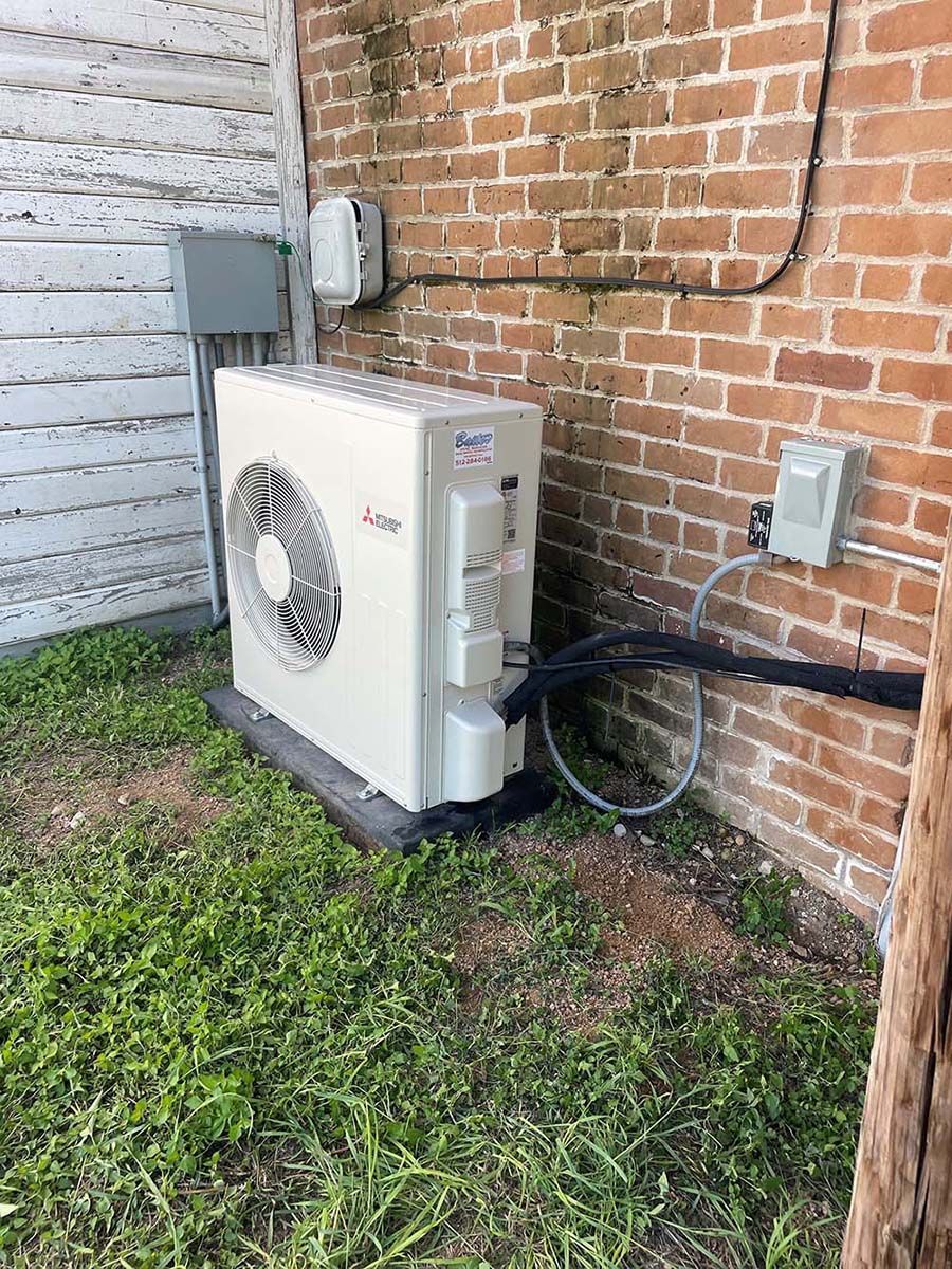 A white air conditioner is sitting on the side of a brick building.