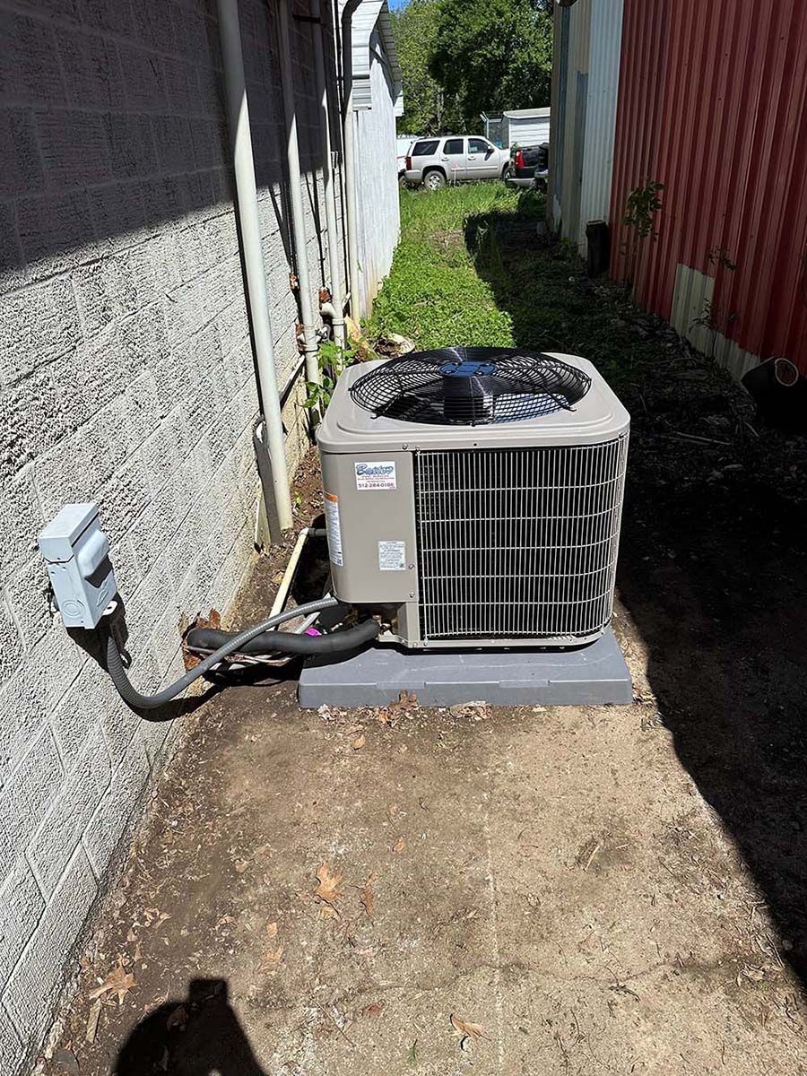 An air conditioner is sitting on the ground next to a wall.