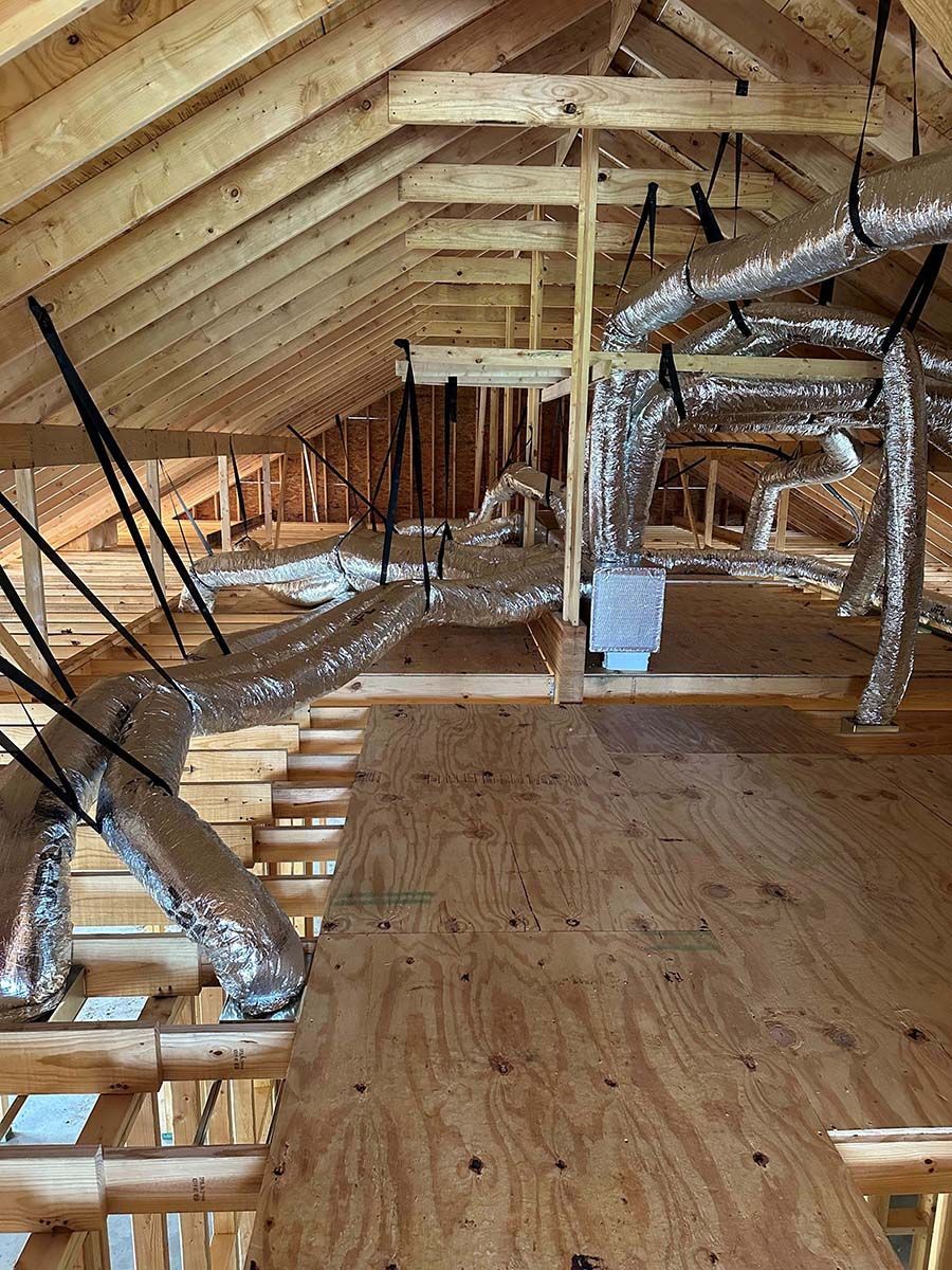 The attic of a house under construction with a lot of pipes hanging from the ceiling.