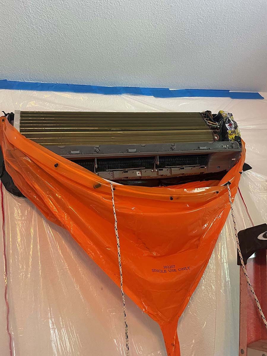 An air conditioner is being cleaned with an orange bag