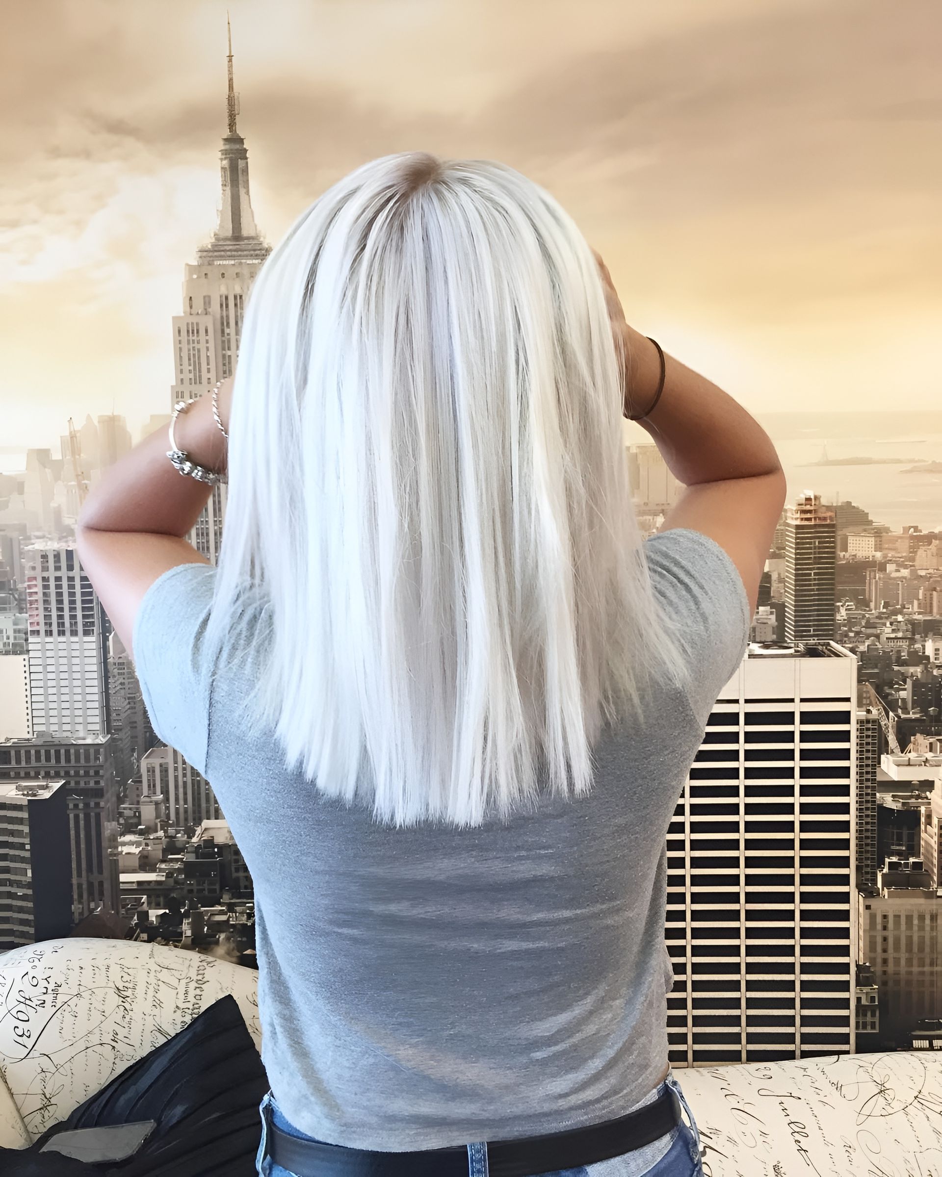 A person with bright white hair, seen from behind, standing in front of a New York City skyline mural.