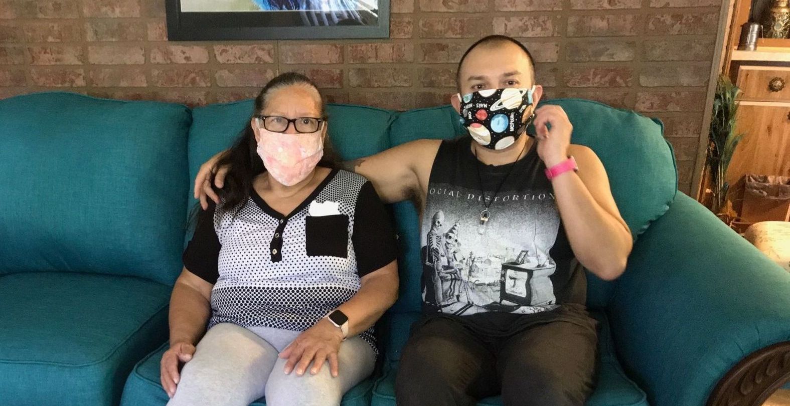 A man and a woman wearing face masks are sitting on a couch.
