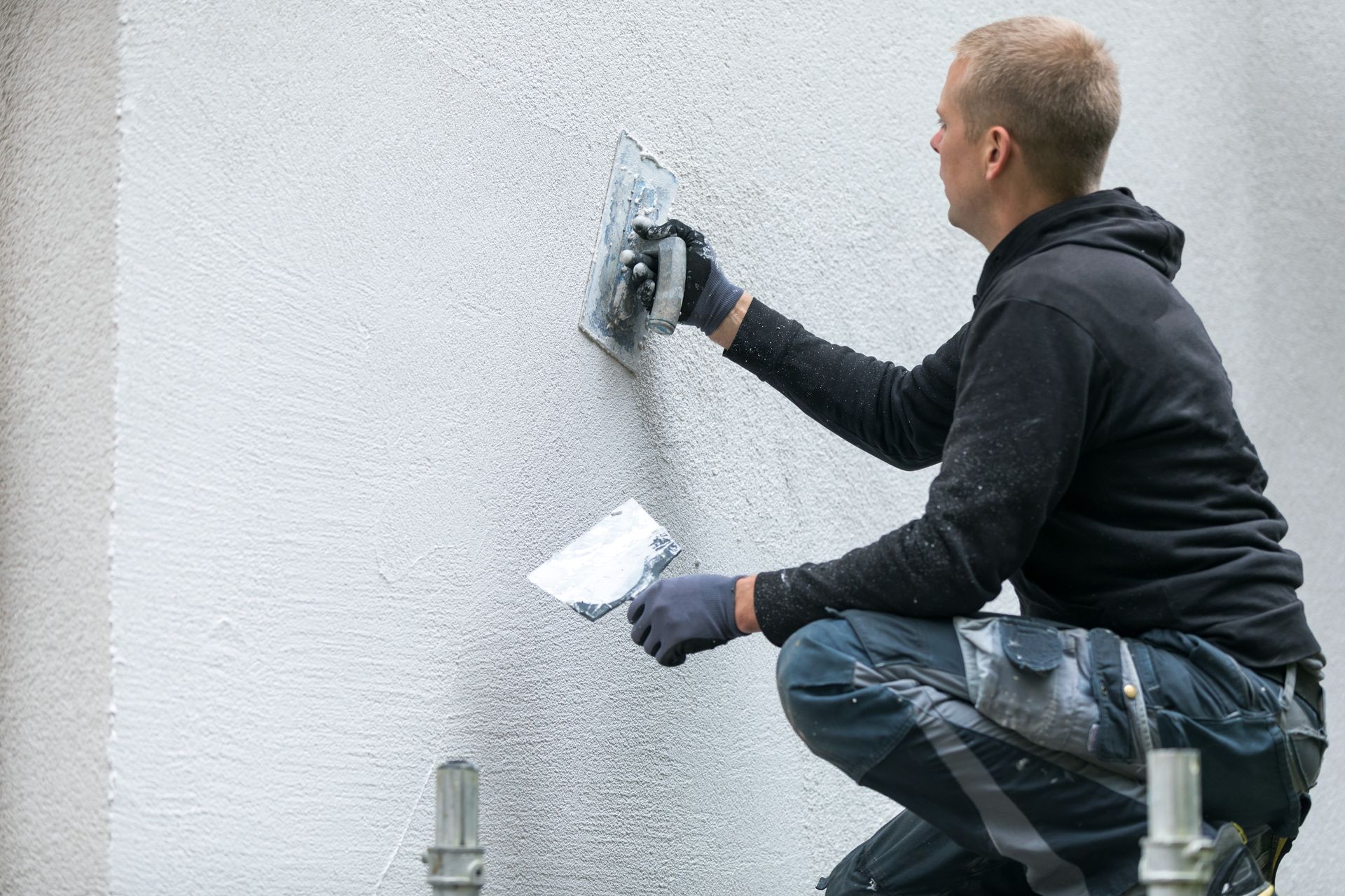 Un homme applique du plâtre sur un mur extérieur à l'aide d'une truelle.