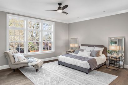Chambre avec grandes fenêtres, murs gris, lit, chaise longue et tapis.