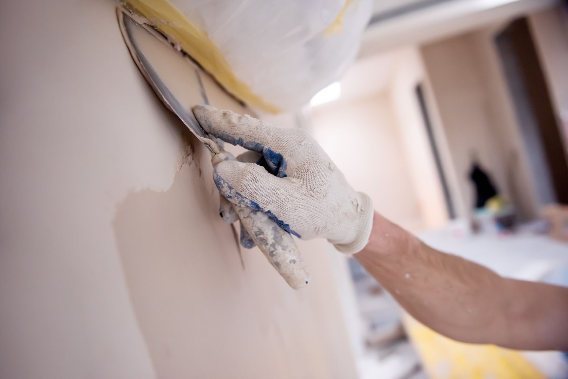 Lissage manuel du plâtre sur un mur avec une truelle ; personne portant des gants, environnement intérieur.