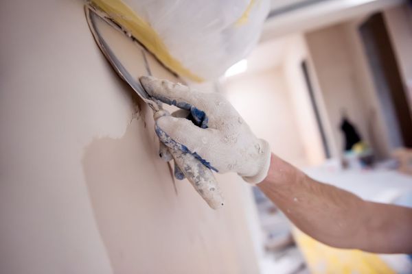 Lissage manuel du plâtre sur un mur avec une truelle ; personne portant des gants, environnement intérieur.