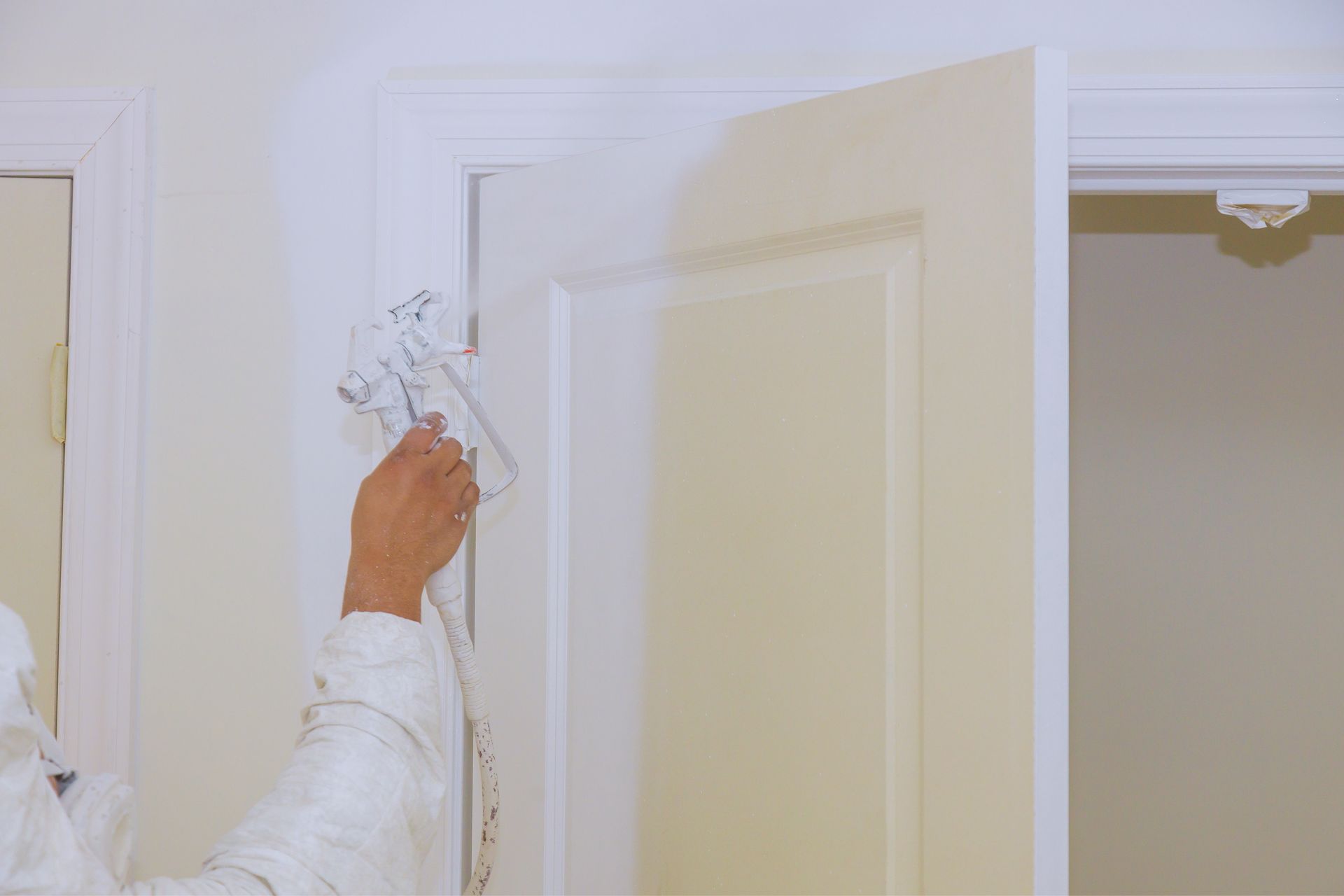 Une personne en blanc peint une porte, pulvérisant de la peinture blanche.
