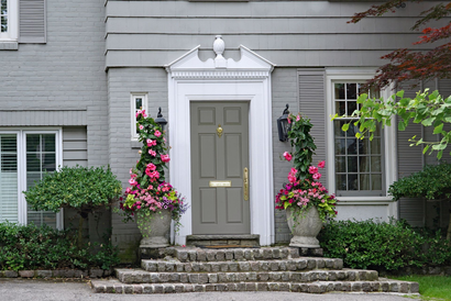 Maison grise avec porte grise, marches et jardinières avec des fleurs roses.