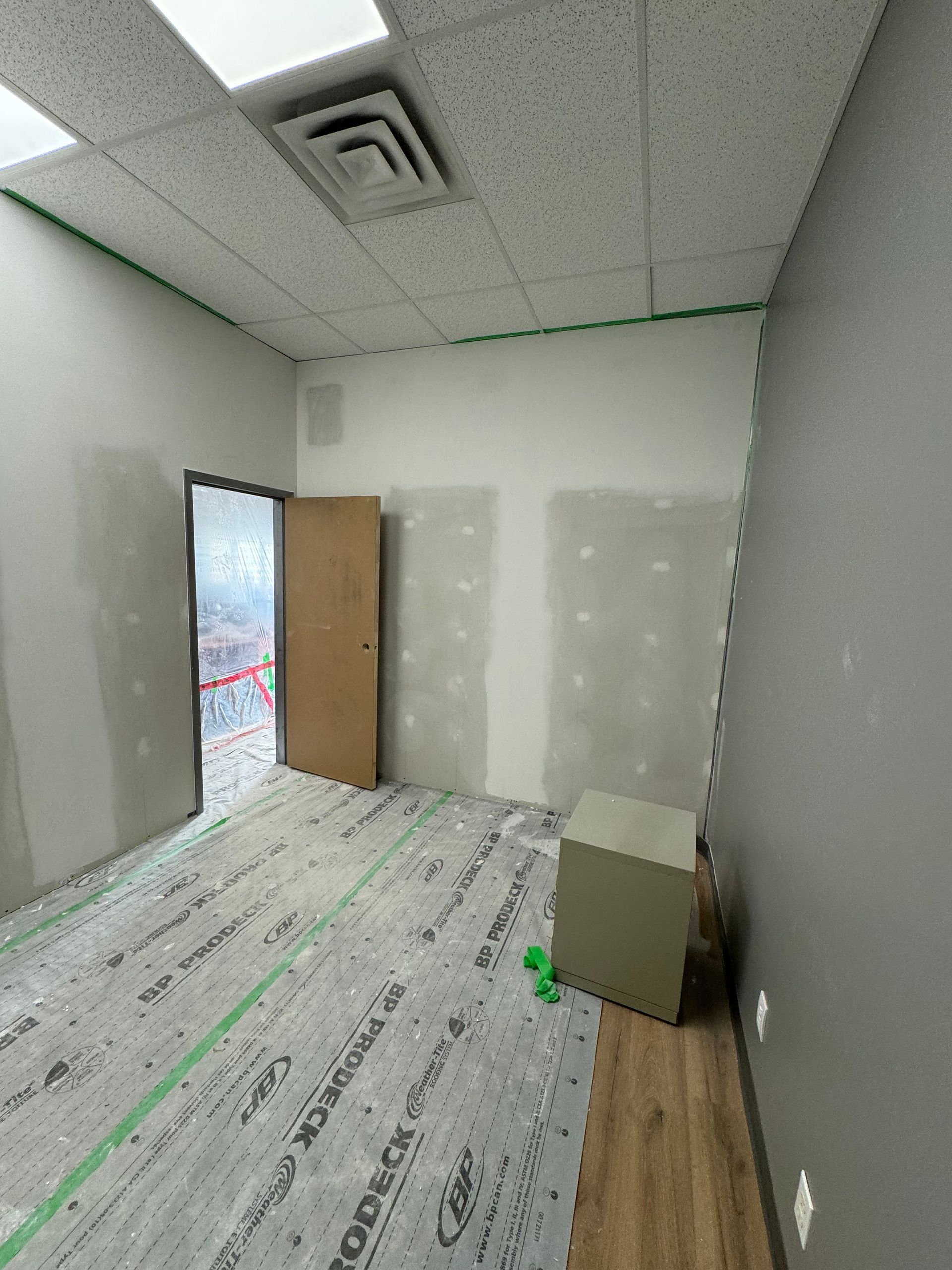 Une pièce vide en construction avec des cloisons sèches, du parquet et une porte.