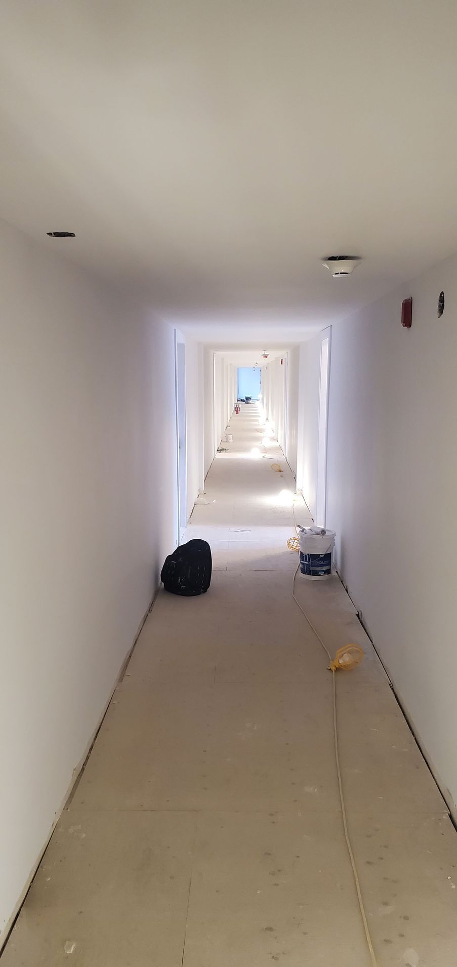 Un long couloir blanc en construction avec un sac noir et un pot de peinture.