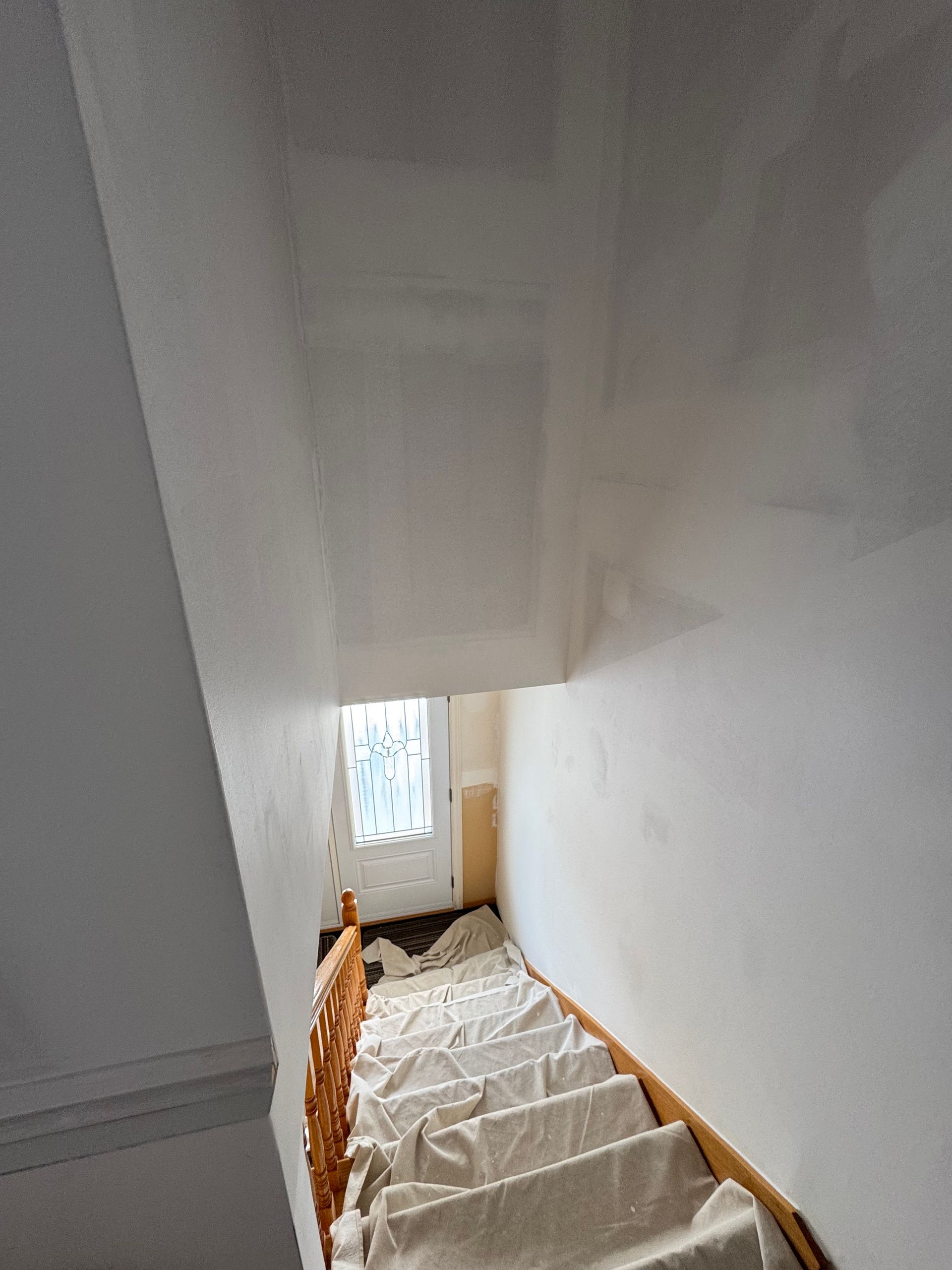 Cage d'escalier aux murs blancs, lumière du soleil provenant d'une fenêtre en bas et revêtements de protection sur les escaliers.