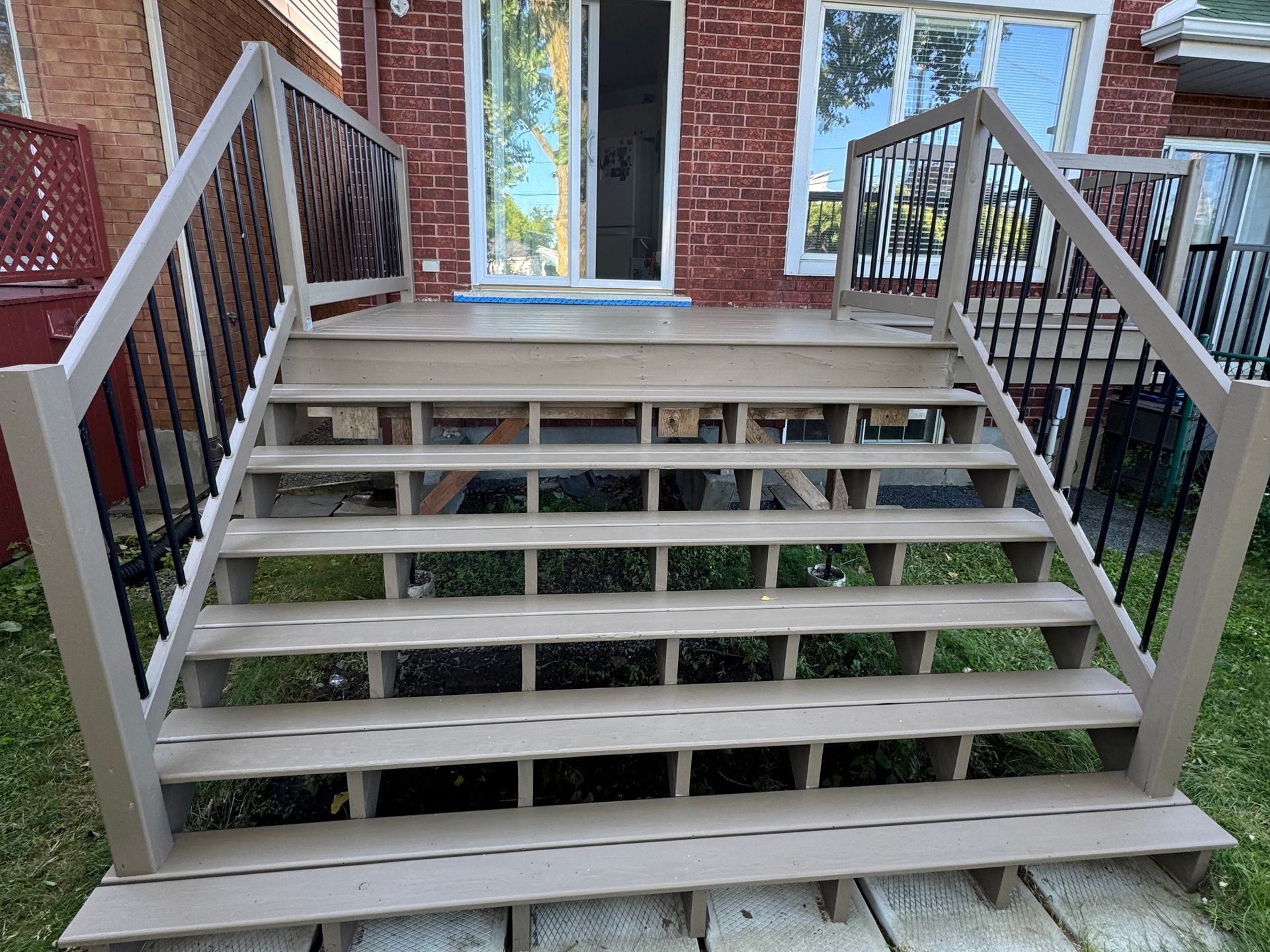 Escalier de terrasse en bois avec rampe marron, menant à une porte coulissante et à une terrasse.