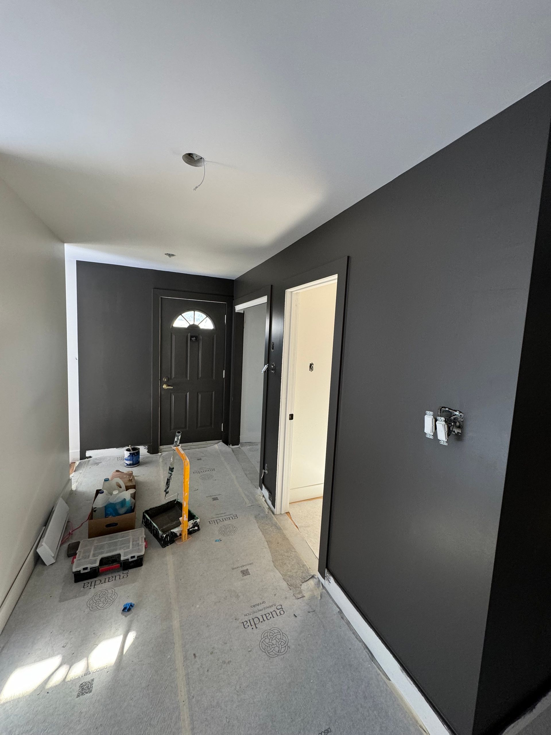 Couloir en construction, murs gris foncé, plafond gris, porte foncée, outils au sol, sol en béton.