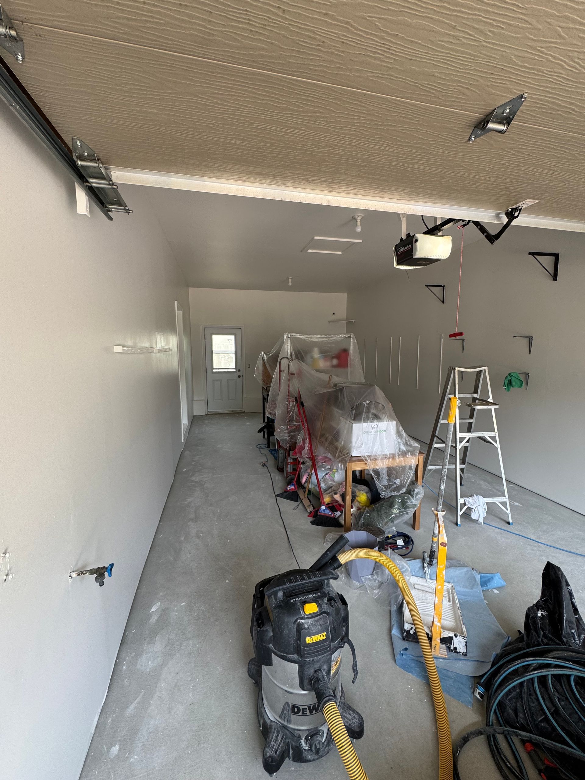 Intérieur d'un garage avec sol en béton et murs blancs. Un aspirateur est au premier plan.
