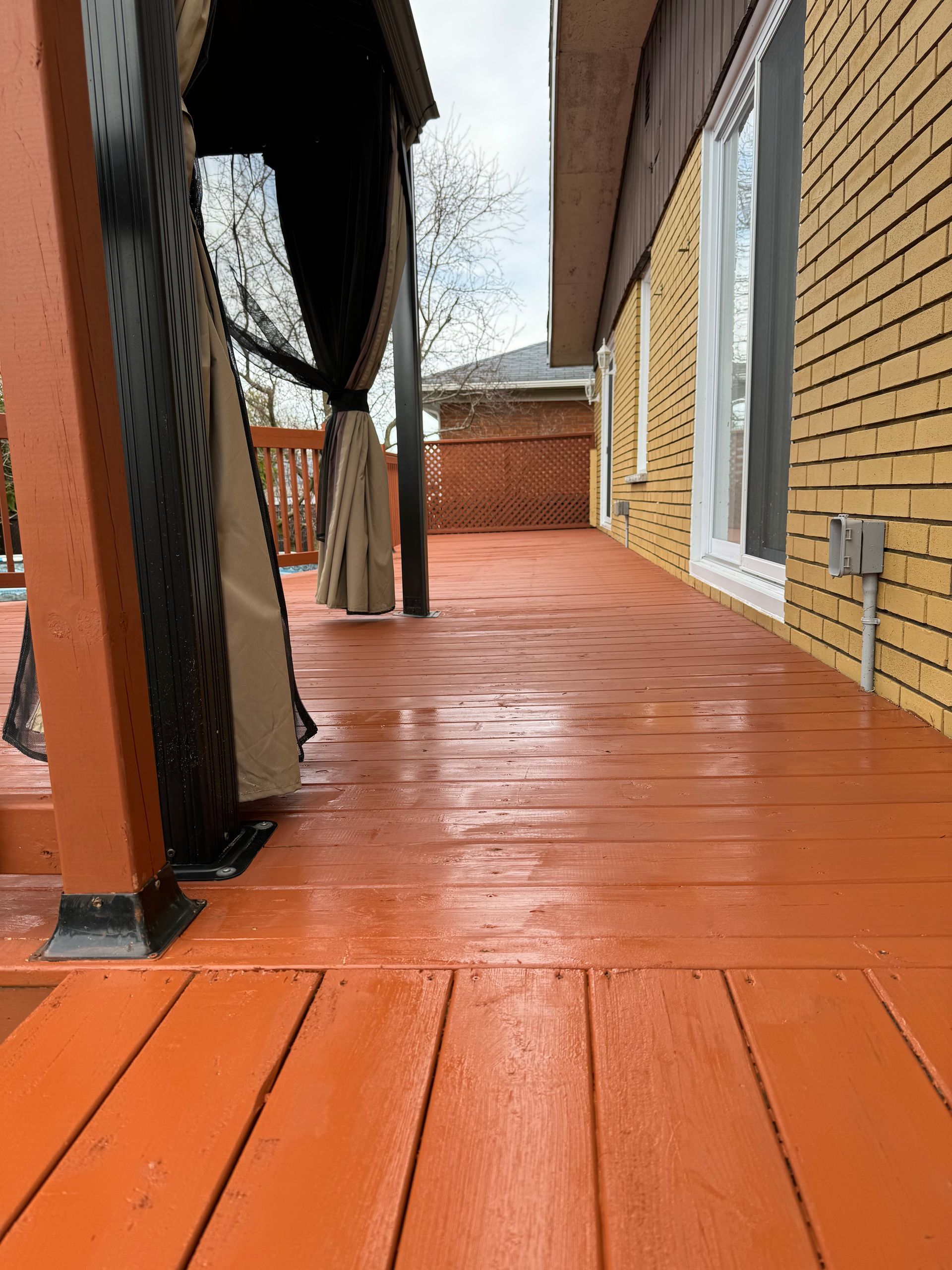 Une terrasse en bois peinte en orange s'étend de gauche à droite, à côté d'un bâtiment en briques jaunes, avec un belvédère sur la gauche.