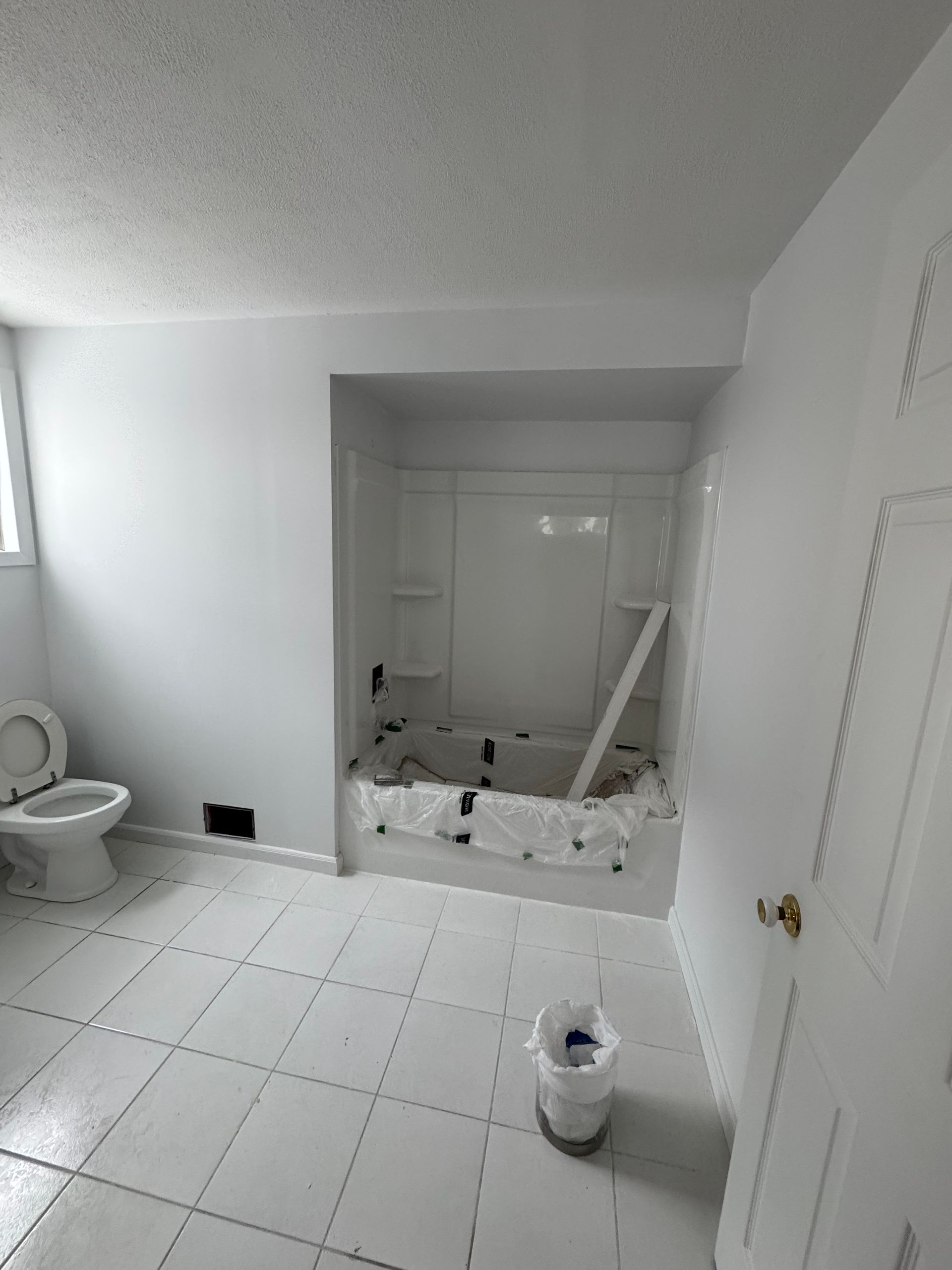 Salle de bain blanche avec toilettes, douche/baignoire et porte fermée.