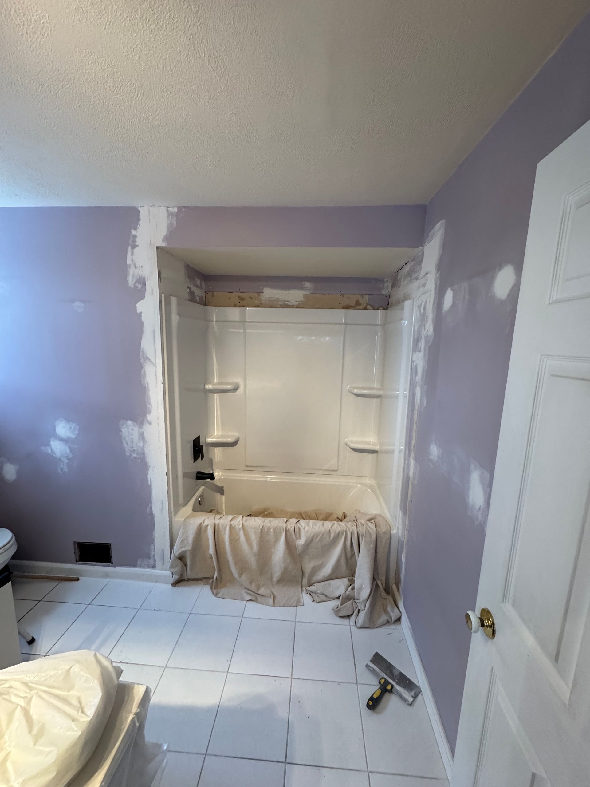 Salle de bain avec murs lilas, baignoire blanche et sol carrelé en cours de rénovation.