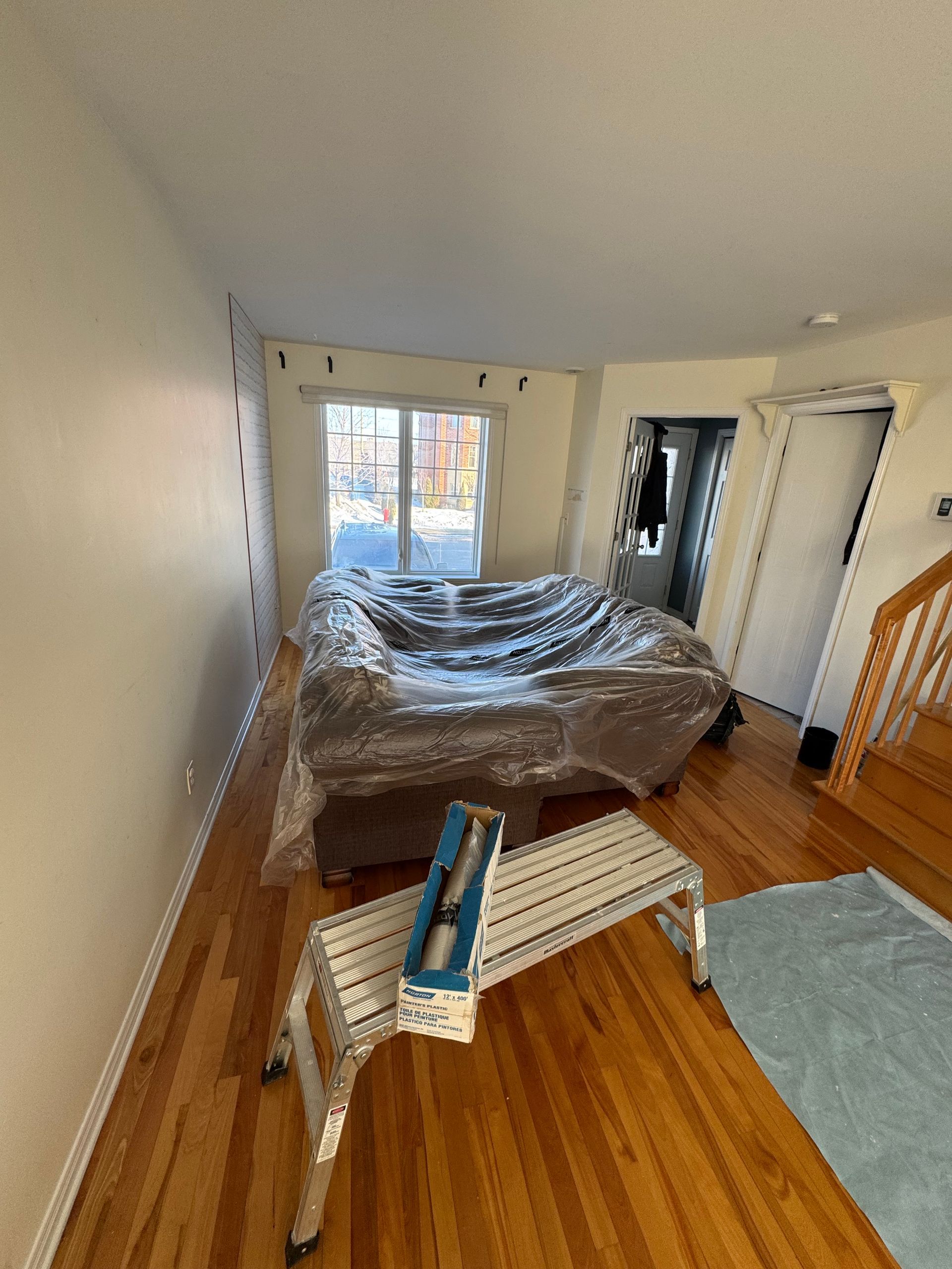 Séjour avec canapé couvert, escabeau, parquet et fenêtre.