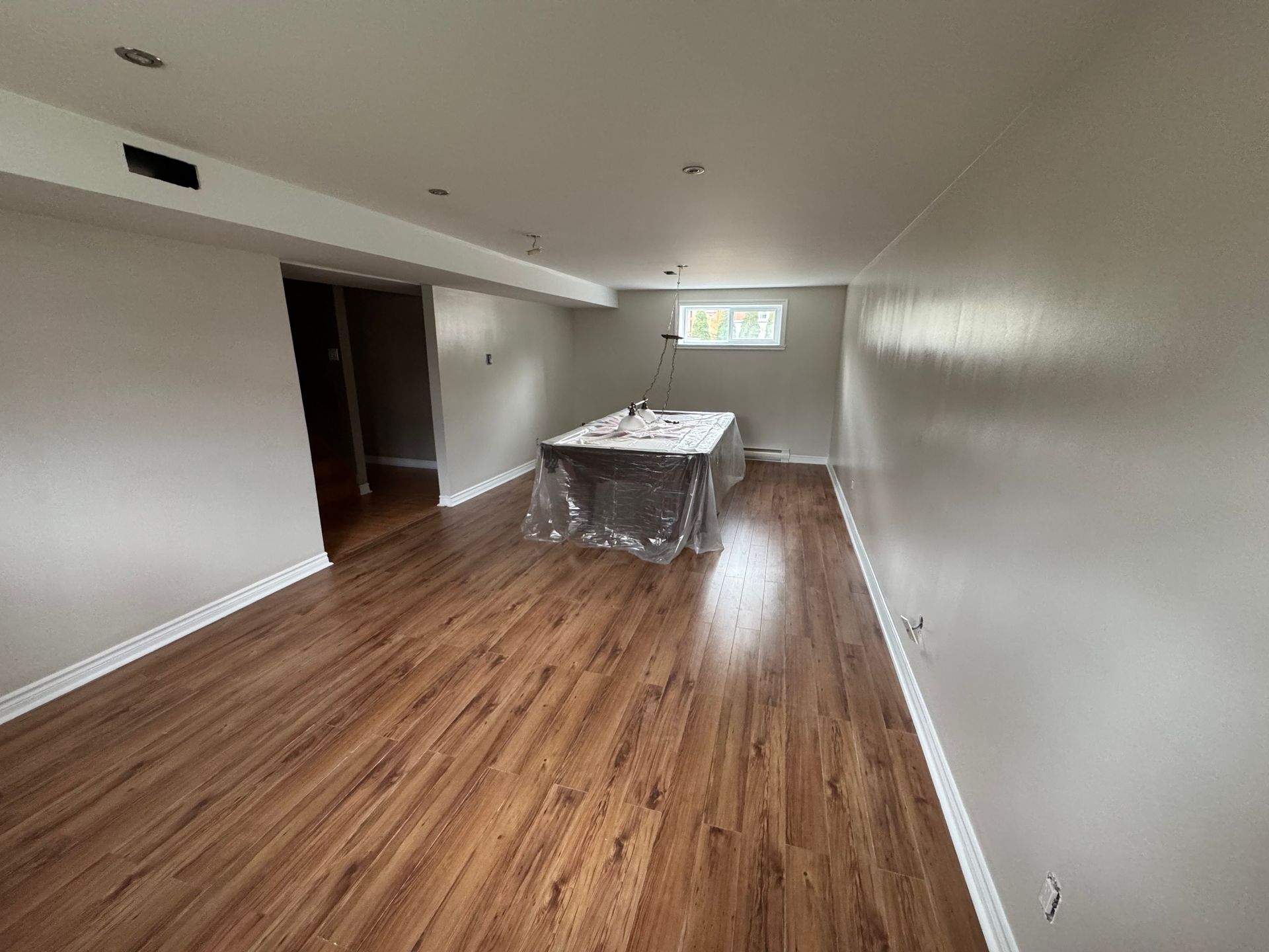 Sous-sol fini avec plancher imitation bois, murs gris fraîchement peints et une table couverte.
