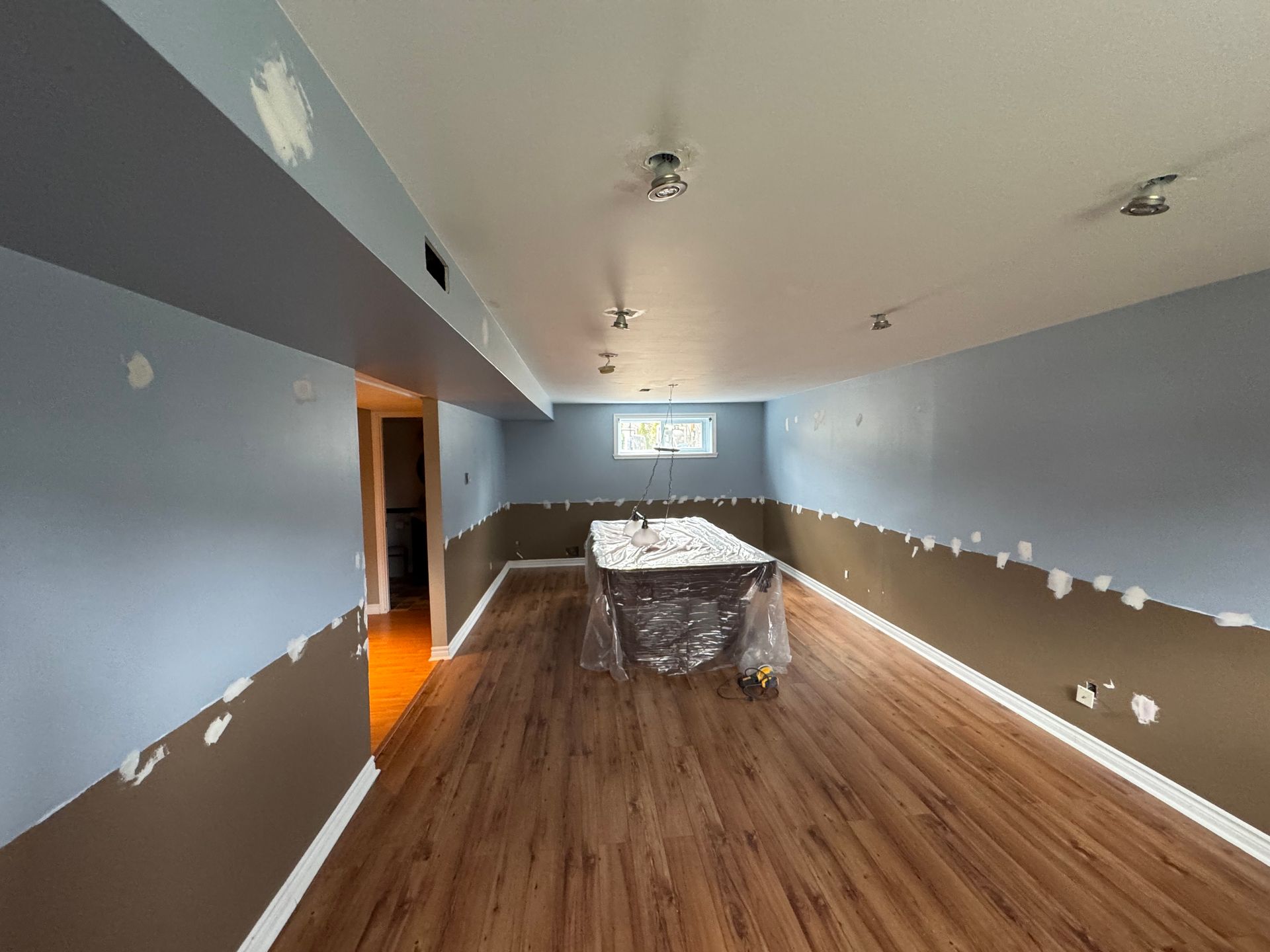 Une pièce avec des murs bleus et marron fraîchement peints, du parquet et une table recouverte de plastique.