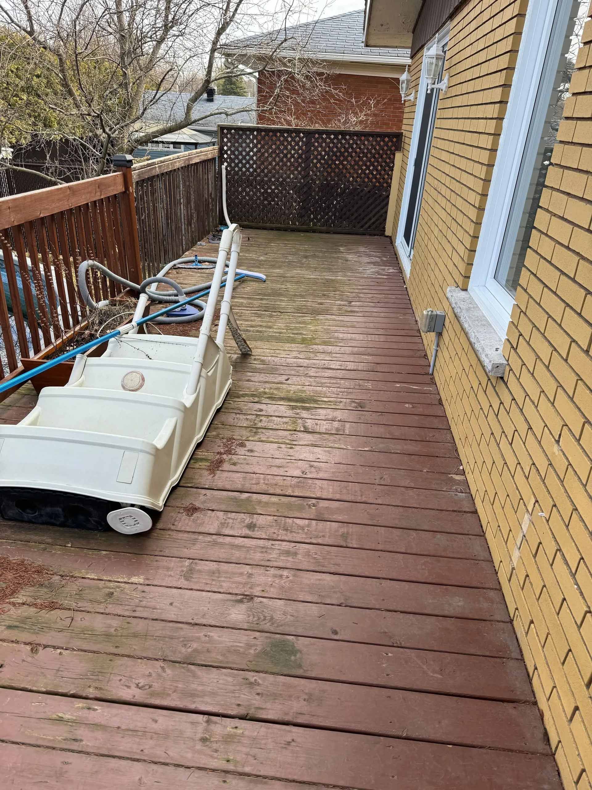 Terrasse en bois avec marches de piscine, contre un mur de briques jaunes et une clôture marron.