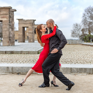 Coppia che balla il tango, lei con un abito rosso, lui con un abito nero, vicino a un'antica struttura in pietra.