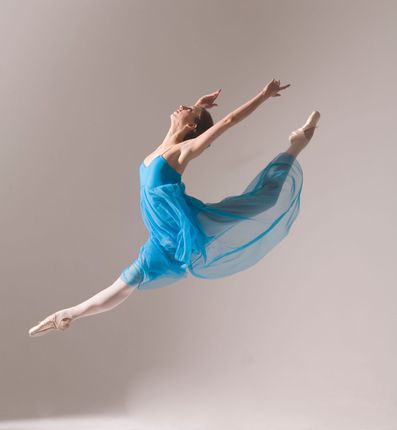 Ballerina in spaccata a mezz'aria, braccia alzate, indossa un abito blu e scarpe da punta.