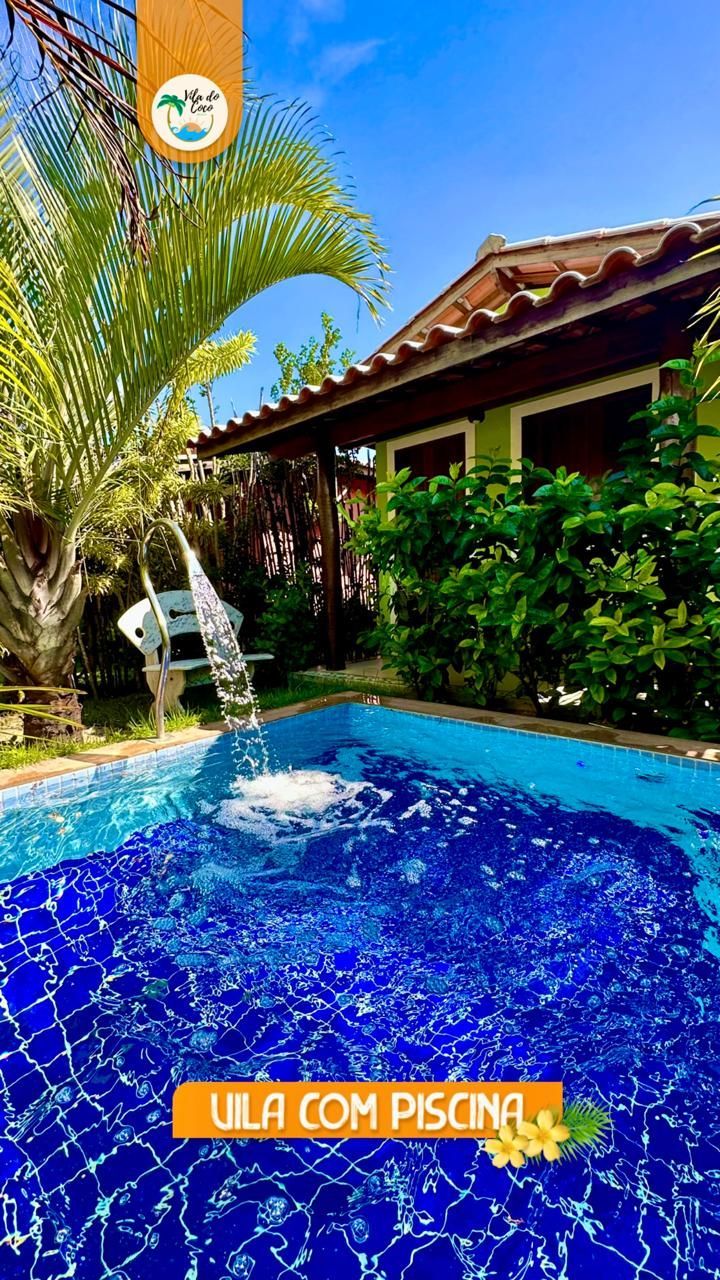 Uma piscina ensolarada com uma cascata e uma casa de férias de madeira ao fundo.