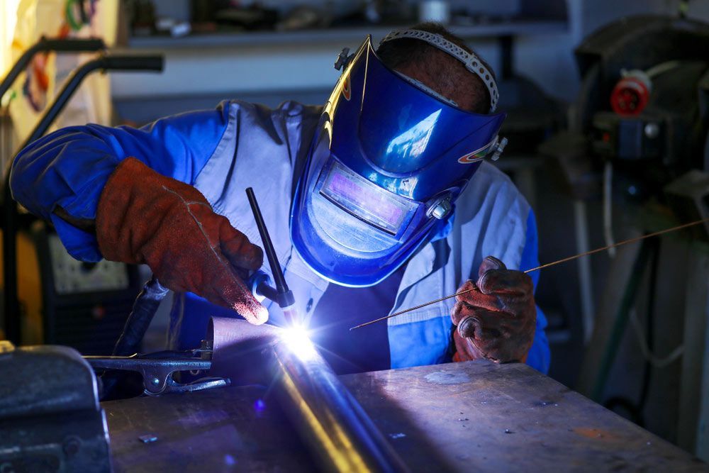 A Man Wearing A Welding Mask Is Welding A Metal Pipe — Brumb's Welding & Fabrication in Biggera Waters, QLD