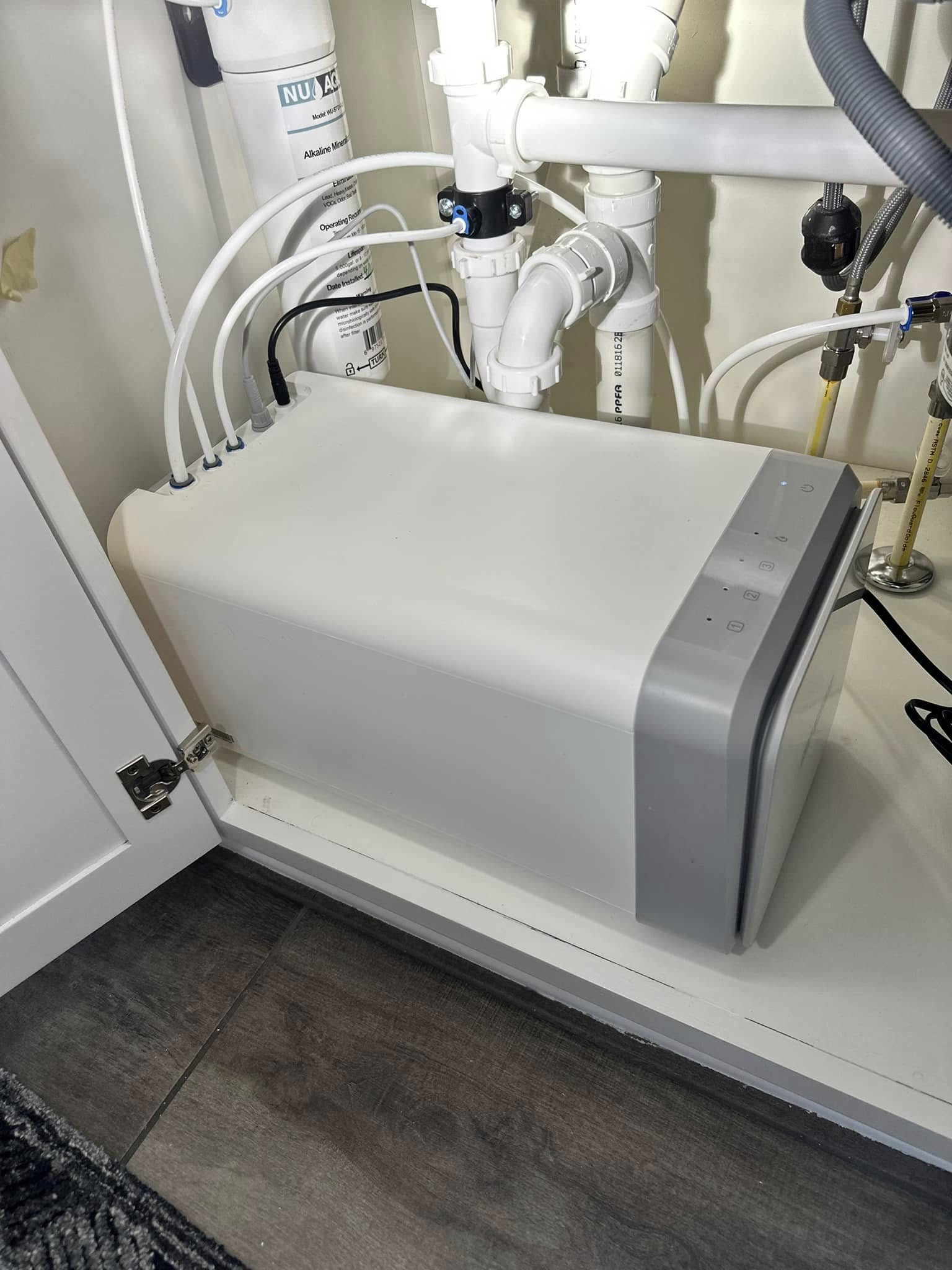 White water filtration system under a kitchen sink, with white pipes and fittings.