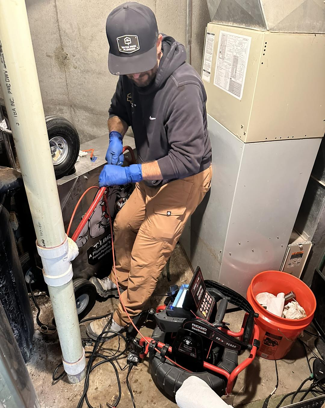 Man in work clothes working on machinery in a basement, wearing gloves.