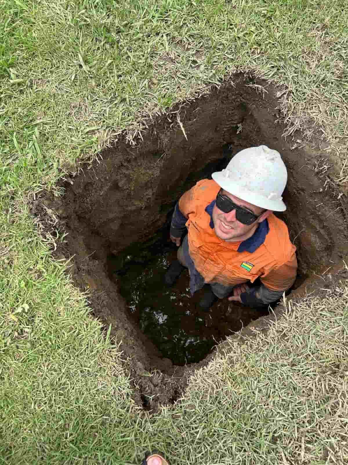 A Man Wearing A Hard Hat And Sunglasses Is Standing In A Hole In The Ground — MCR Hydro Excavations & VAC Truck Services In Belmore River, NSW
