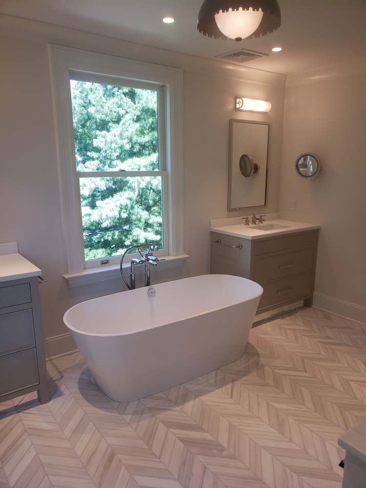 A bathroom with a bathtub , sink , mirror and window.