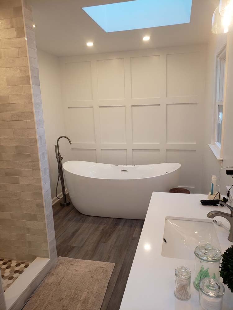 A bathroom with a tub , sink , shower and skylight.