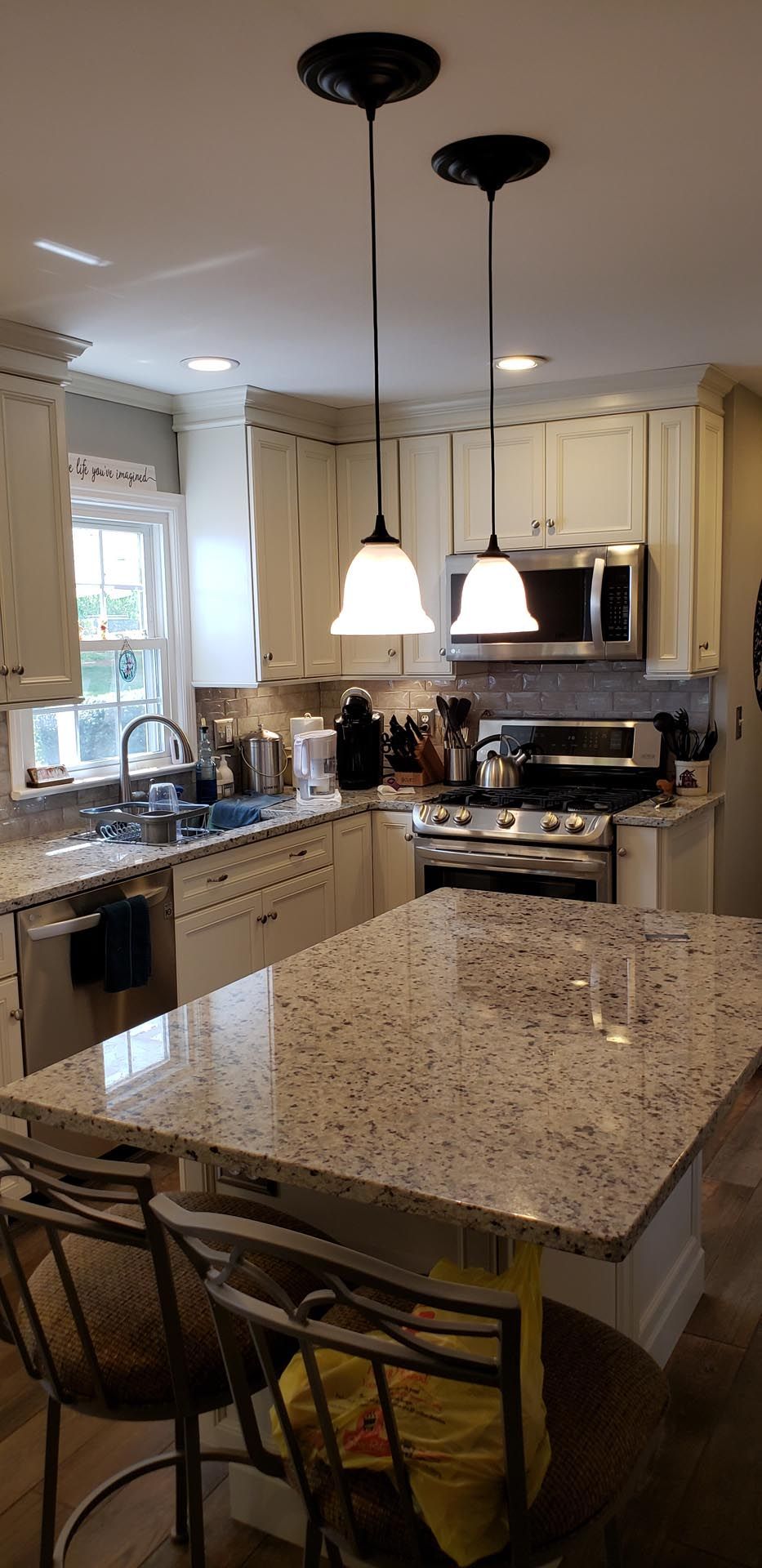 A kitchen with white cabinets , granite counter tops , stainless steel appliances and a large island.