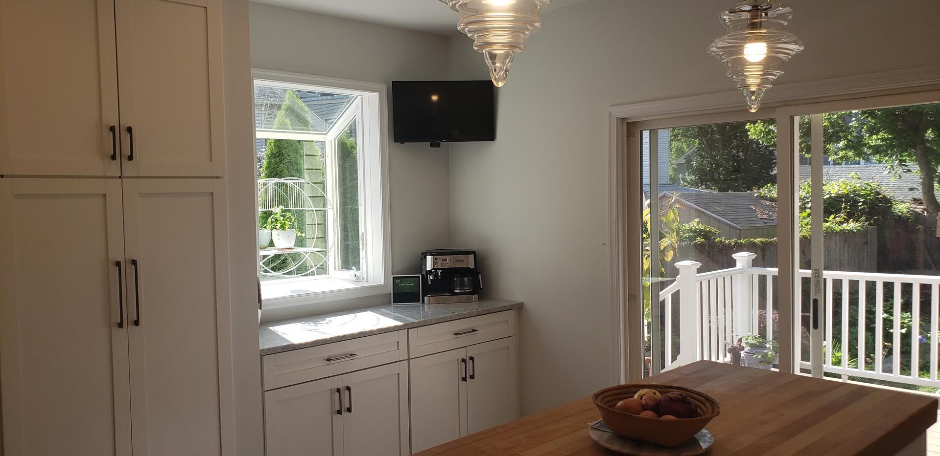 A kitchen with white cabinets , a wooden table and a sliding glass door.