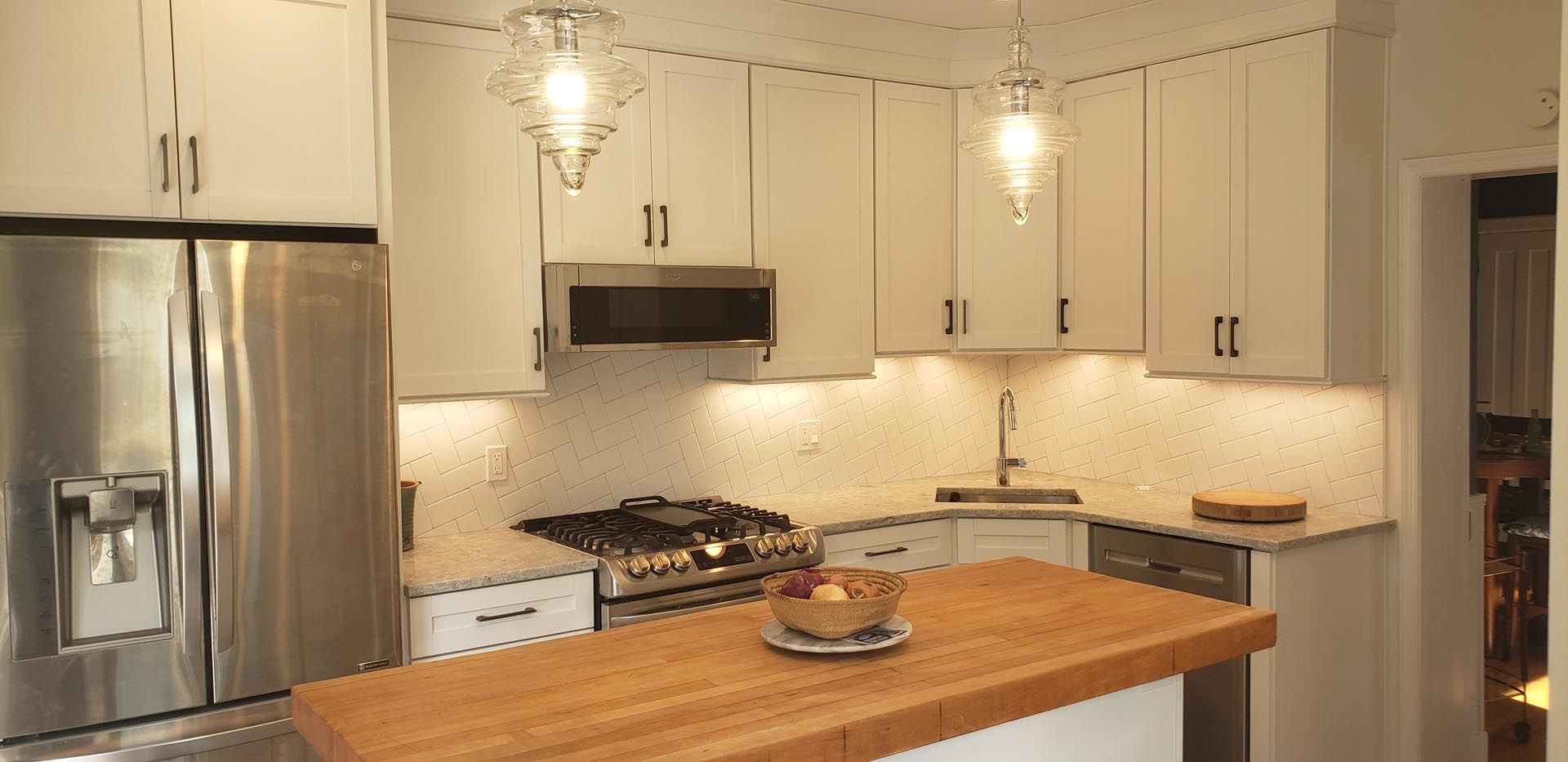 A kitchen with white cabinets , stainless steel appliances and a wooden counter top.