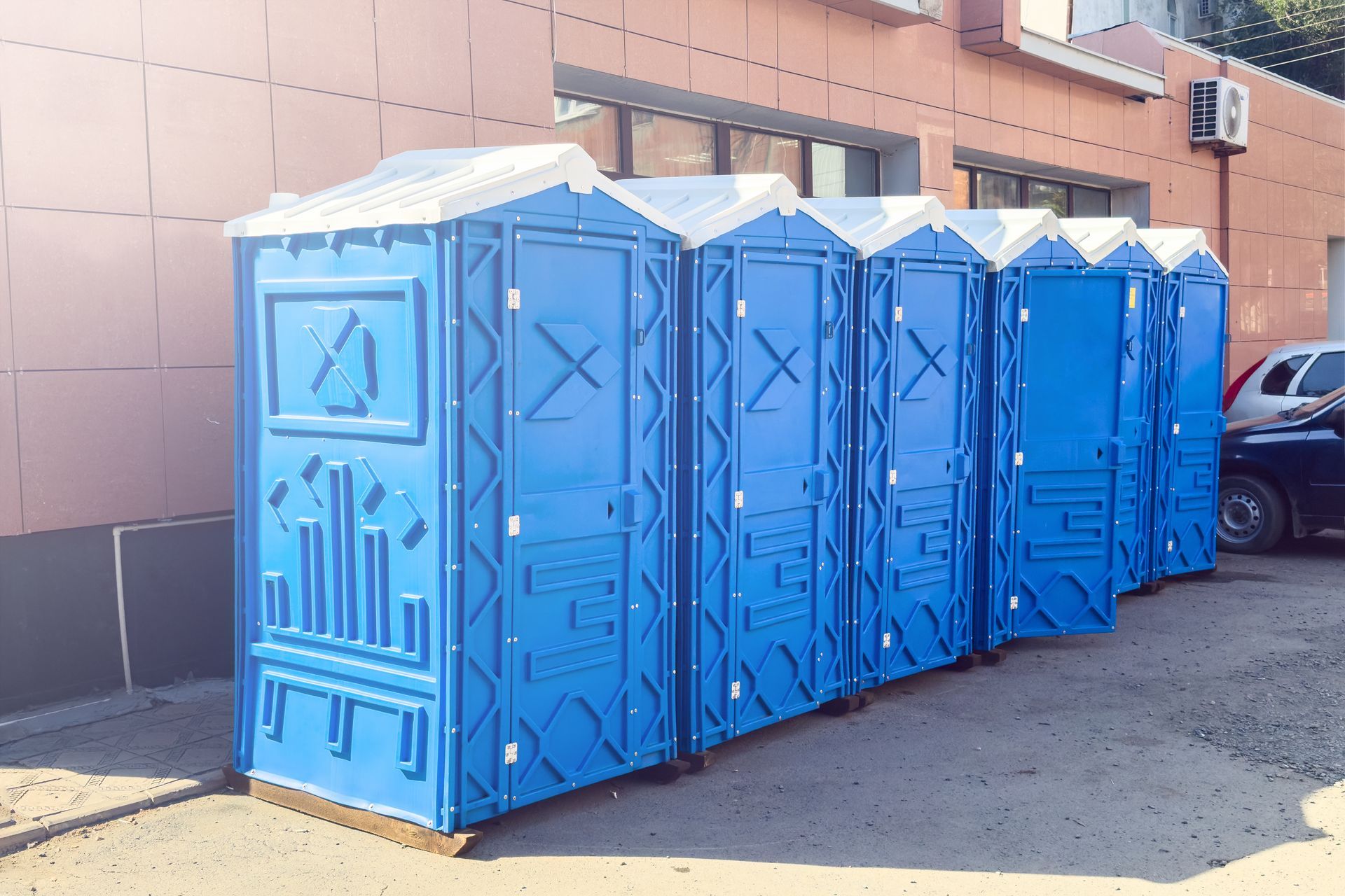 Long line of blue portable toilets stands neatly building wall in an urban setting.
