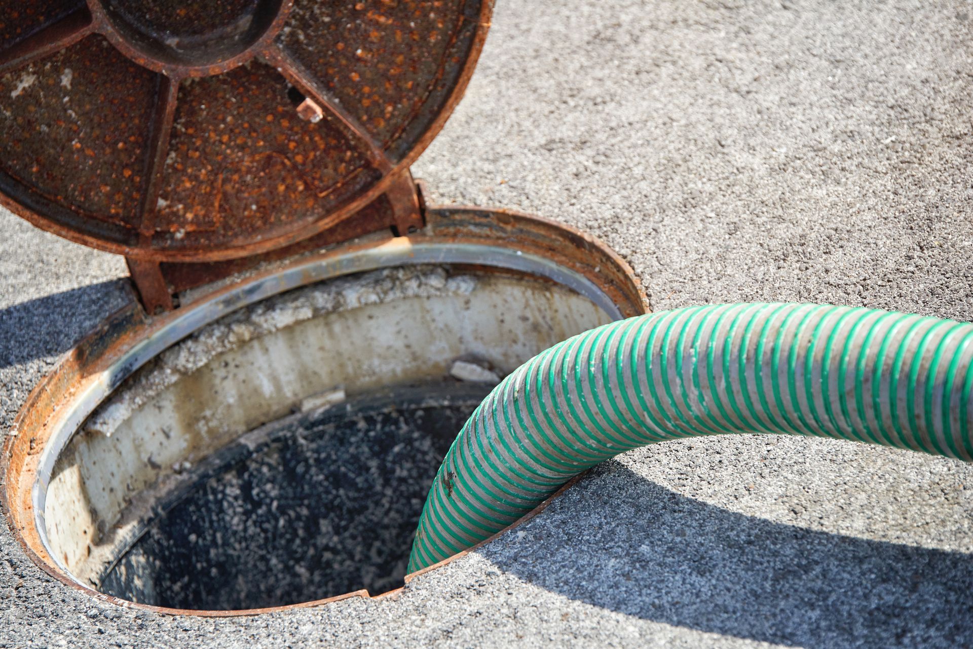Septic tank cleaning with green hose inserted into open manhole for waste removal service.