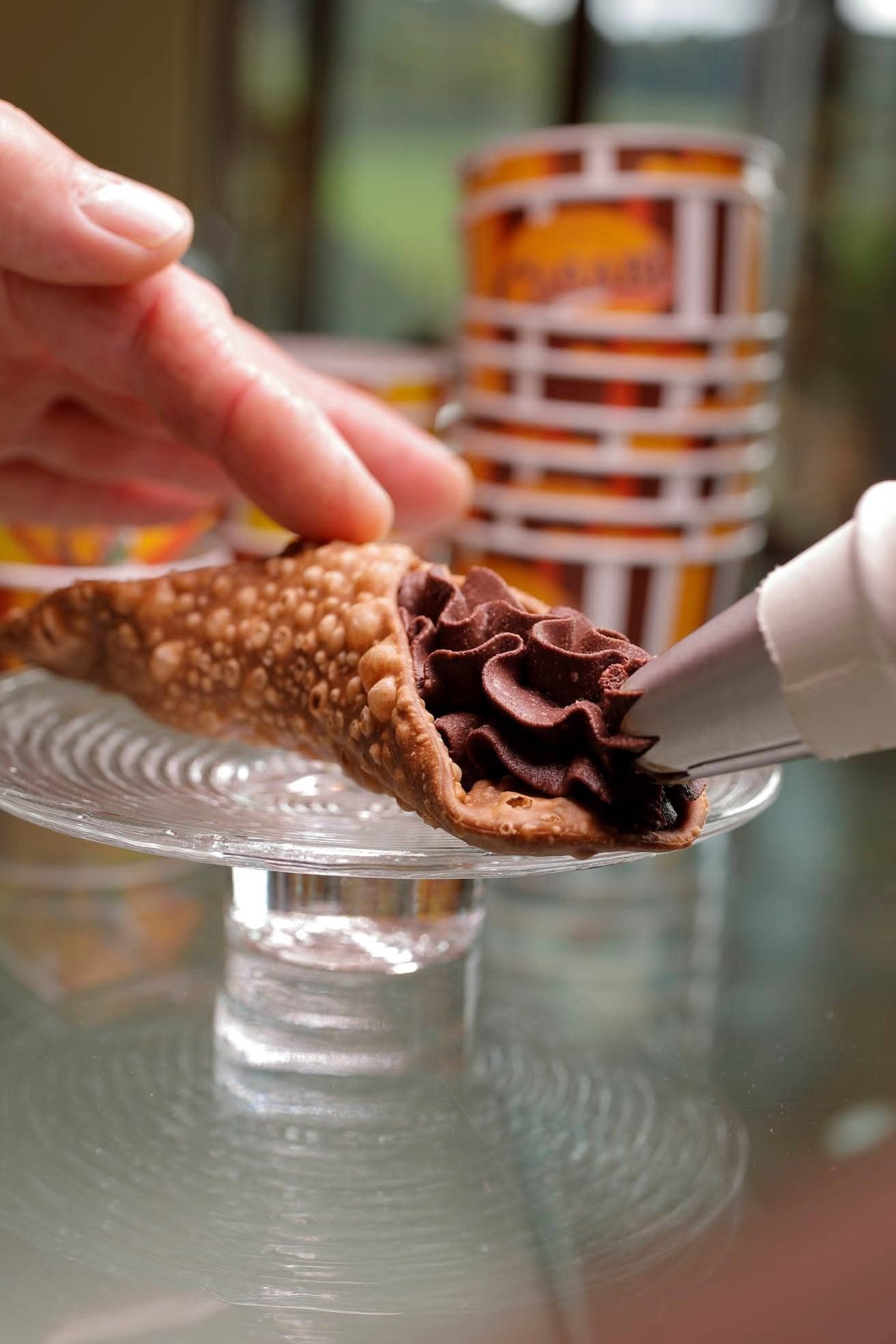 Una persona sta decorando un cannolo con glassa al cioccolato.