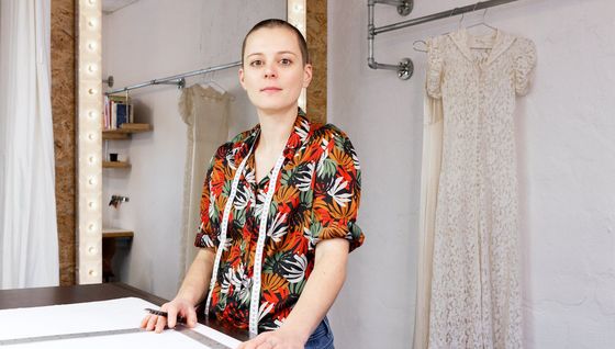 Schneiderin in ihrer Werkstatt, im Hintergrund ein Spiegel und eine Stange mit Brautkleidern