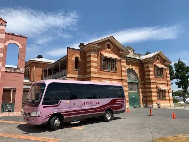 A Pink Bus is Parked Out The Front A Big Brick Building — Wests National Coaches In Chevallum, QLD