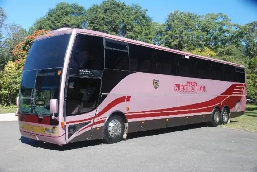 A Pink Bus Parked Outside With Trees Behind It — Wests National Coaches In Chevallum, QLD