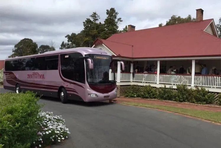 A Pink Bus Parked Infront of A Building With A Red Roof — Wests National Coaches In Chevallum, QLD