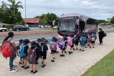 A group of young children in line to get on a coach.