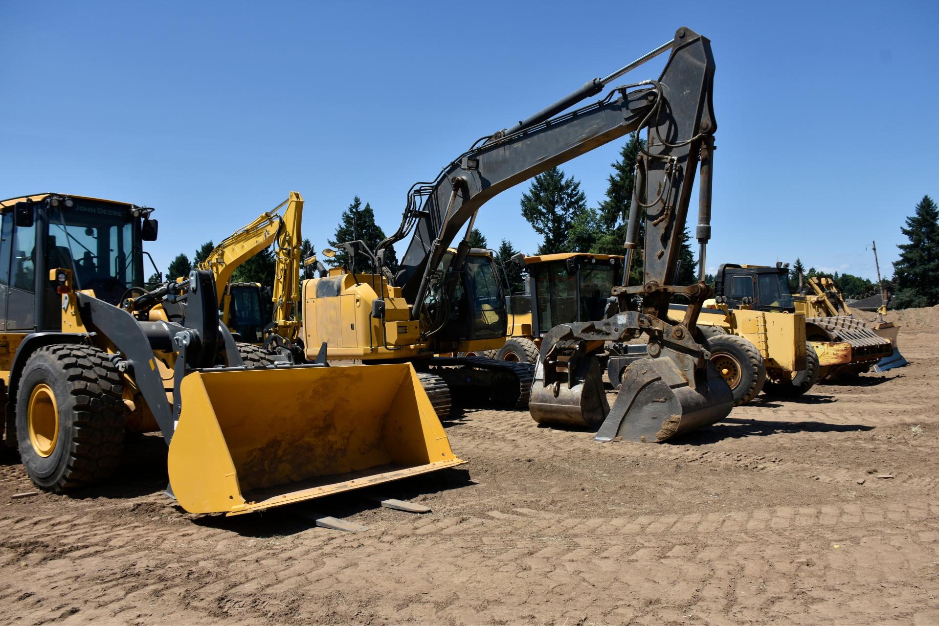 Uma fileira de veículos de construção estão estacionados em um campo de terra.