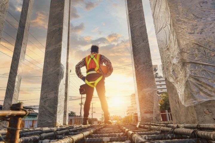 Construction worker on a scaffold at sunset, wearing a safety harness and reflective vest.